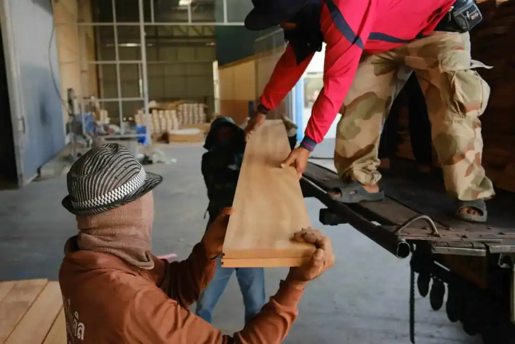 Worker loading wooden plank onto truck at Thaigoodwood facility.